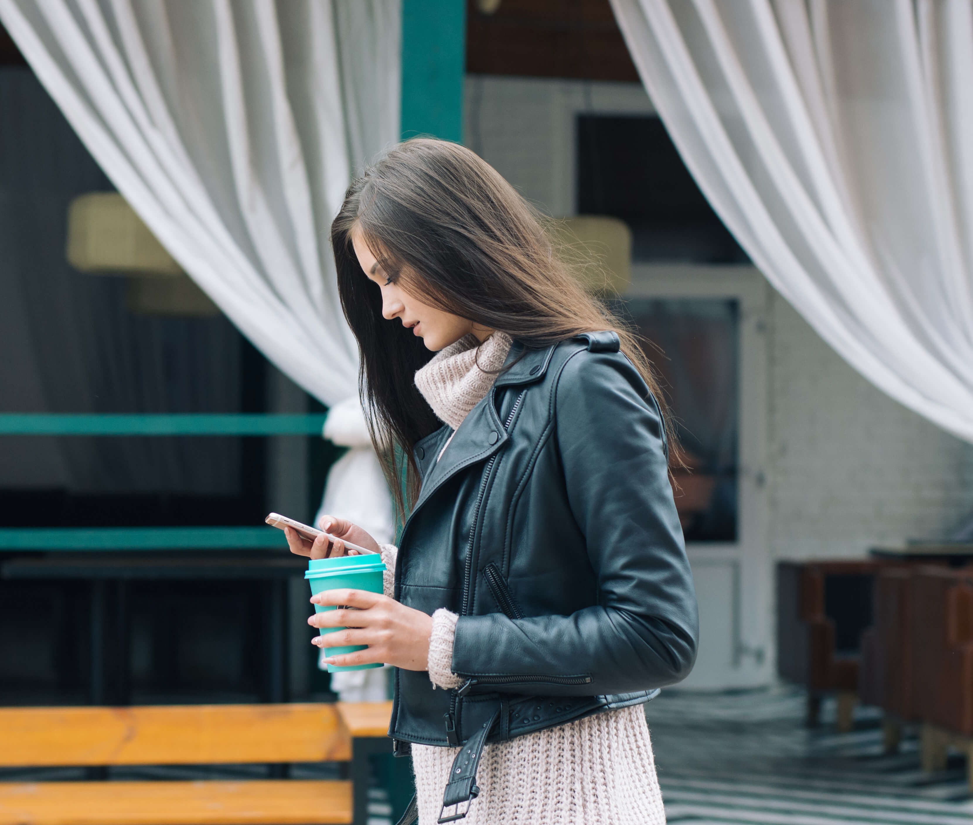 Woman holding coffee in her left hand looking at her phone in her right hand